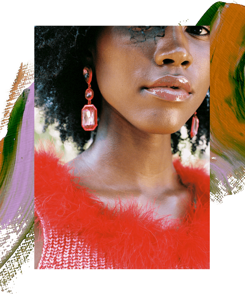 Model Alana January is wearing a pink crop top with a red feather trim. She has pink crystal earrings and her hair is loose and curly. In the second image, she appears with her sister Amaya January, who is wearing a rose-colored tied crop top and has brown curly hair. There is a swatch of purple and green paint behind them.