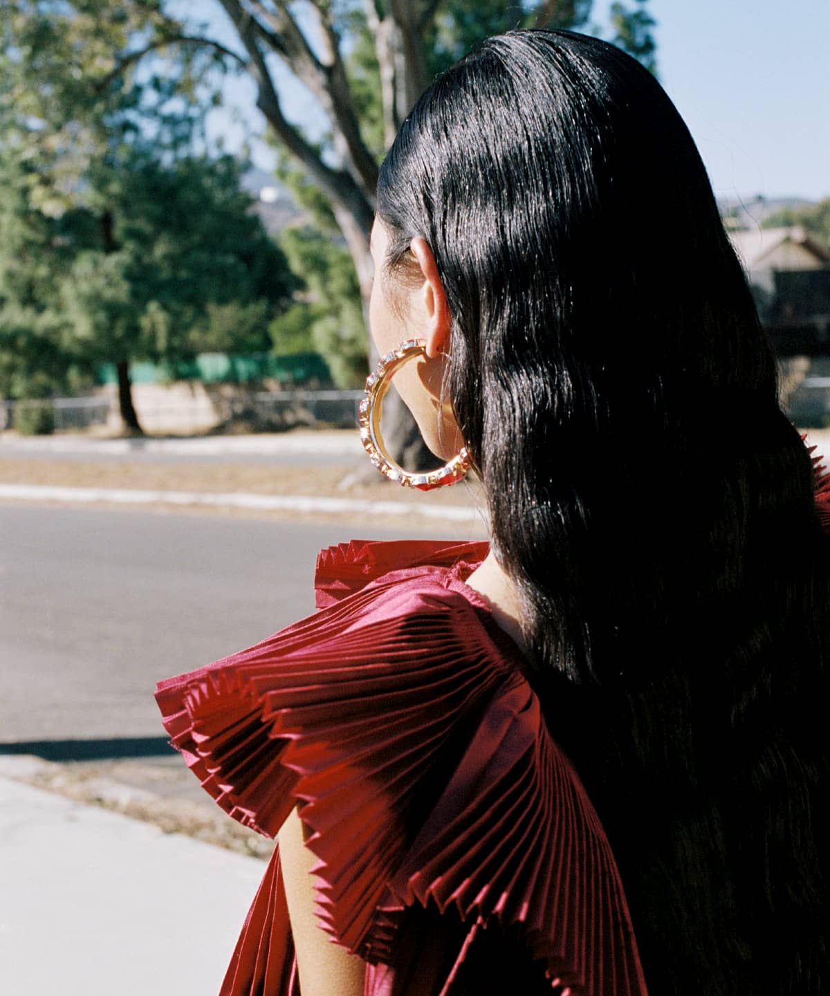 Model Ariel Toole with her back to the camera. She has long wavy brown hair and is wearing a red dress.