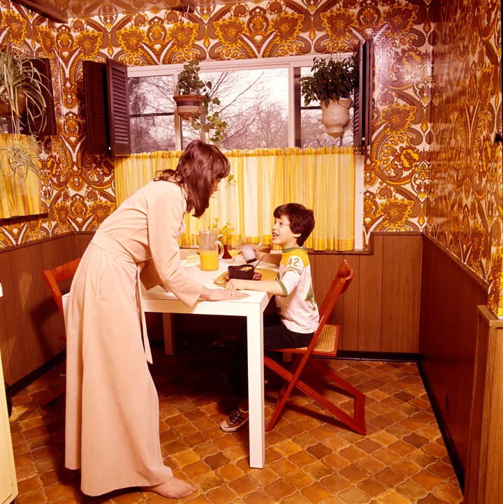 Archival 1970s image of a mother and a son in their orange and brown kitchen. 