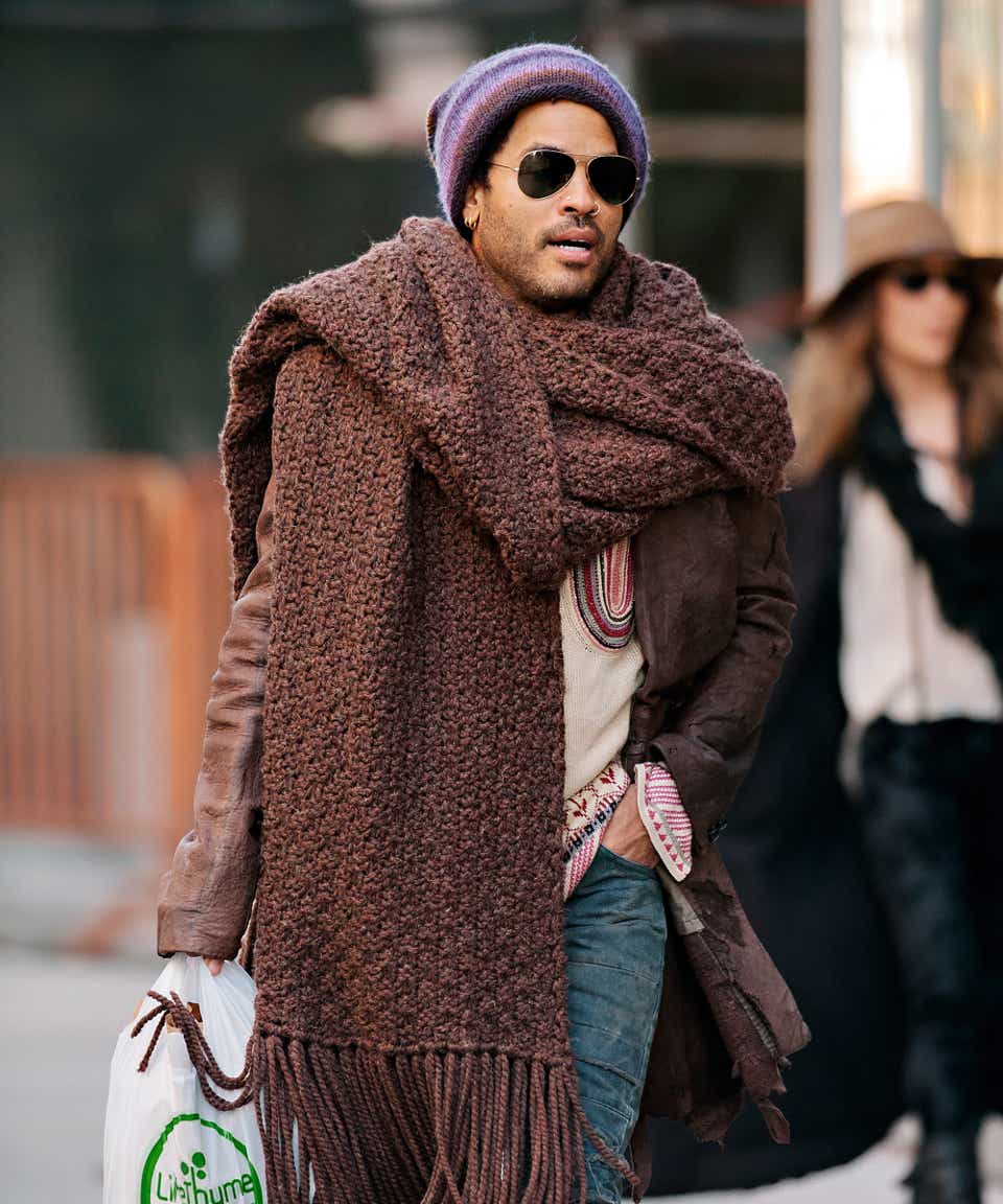 Lenny Kravitz seen wearing colorful beanie and oversized scarf with an embroidered sweater, torn jeans and fringed boots.