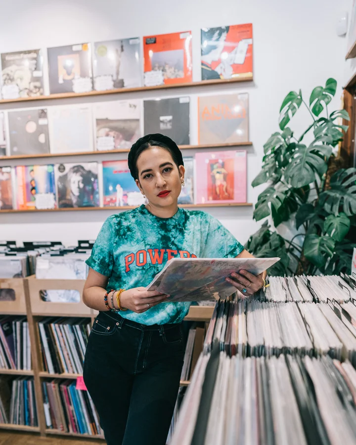 Image of Kim Darragon wearing a Teal tie dye t-shirt with the word Power in red lettering she is holding a vinyl record 
