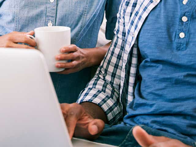 A person holding a mug sitting next to another person on a laptop.
