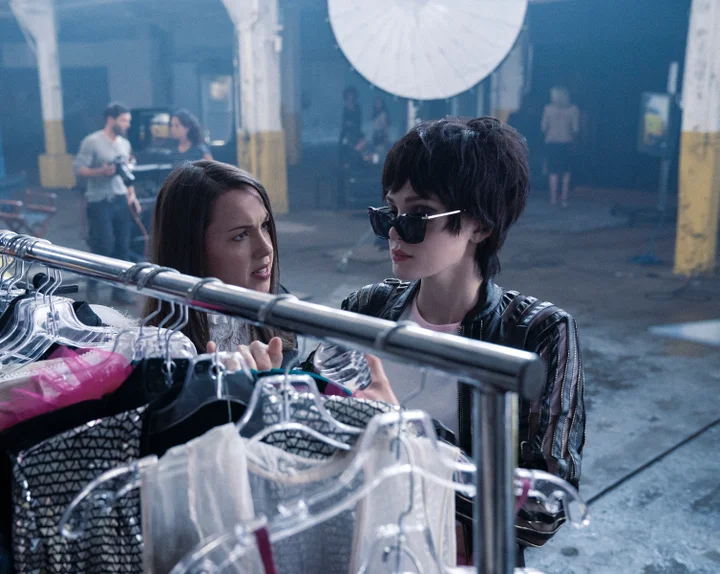 Chloe arrives late and hungover to a photoshoot in a warehouse. She is wearing sunglasses and a leather jacket. 
