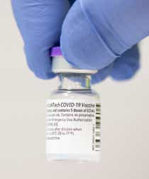 Vaccine vial being held by a hand in blue gloves.