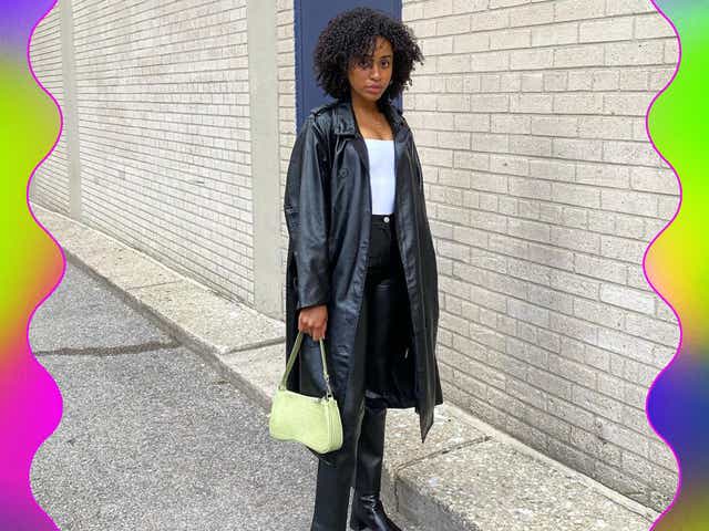 A woman wearing a black tench coat, leather trousers and a green handbag