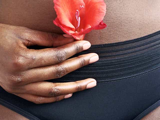 A woman holding an orange flower in front of her stomach