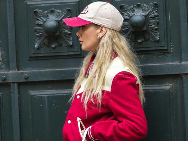 A guest wears a white and red ripped Von Dutch cap, silver earrings, a red and white latte teddy jacket, blue faded high waist flared pants, a white with FF monogram embossed with pink paint pattern handbag from Fendi, white latte leather pointed block heels ankle boots, outside Loewe, during Paris Fashion Week