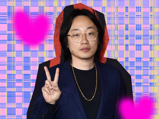 Jimmy O. Yang in a navy suit and gold chain throwing up a peace sign.