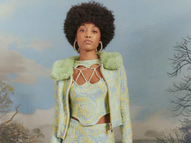 A model wearing a cutout corset top in a pastel green-blue-yellow swirl design with a matching cardigan and pants.