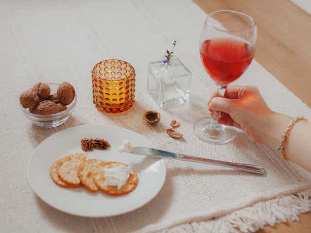 Hand holding a glass of wine next to a snack plate with cheese, crackers and nuts