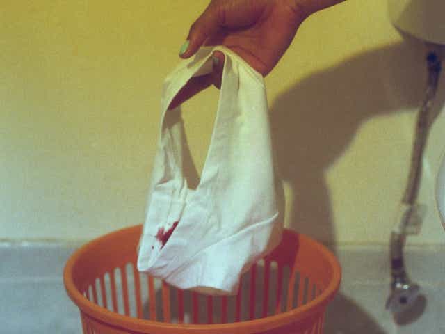 Person holding white underwear with period stains over a red basket.