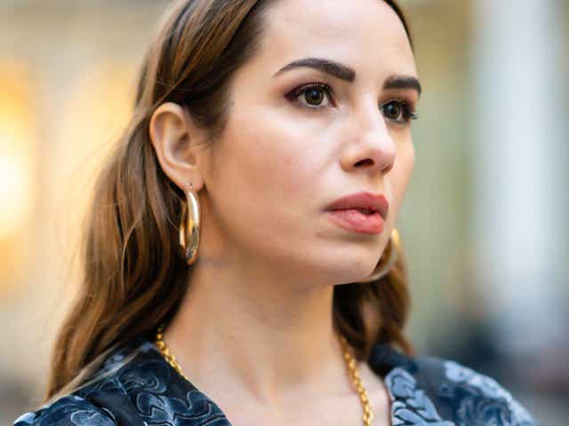 Maria Rosaria Rizzo wears gold earrings, a gold long chain necklace with a large pendant.