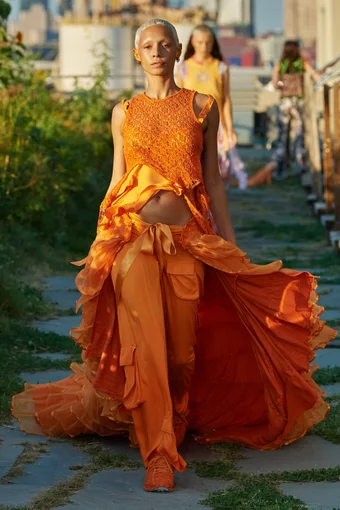 a model wears an orange asymmetric dress with carho pants and matching sneakers at the Collina Strada spring 2022 show