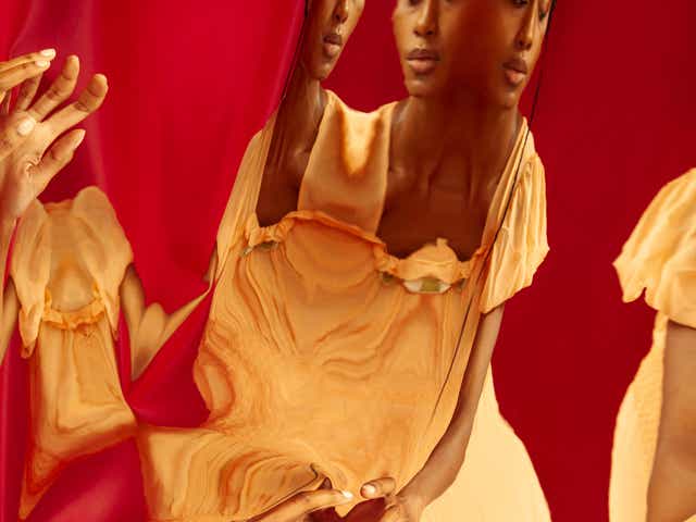 Abstract image of a Black femme person in front of a mirror and red background.