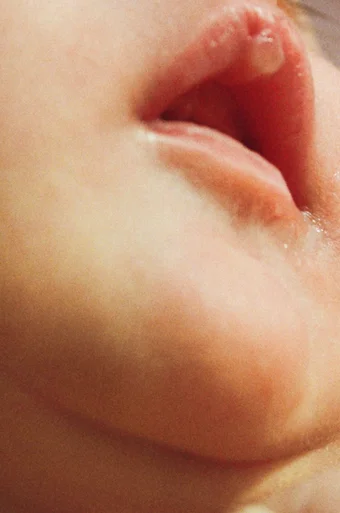 Close up of a newborn baby's open mouth and chin – there is a spit bubble on her upper lip.