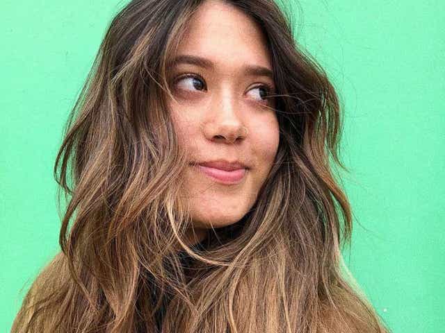 Person with long wavy light brown hair against a green wall