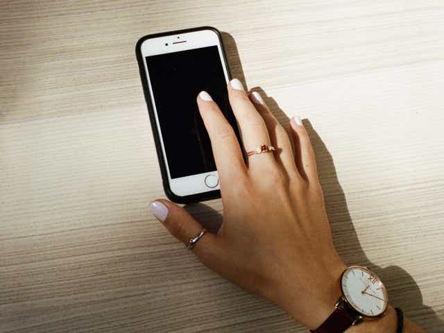A photo of someone holding a smart phone with a watch and ring on