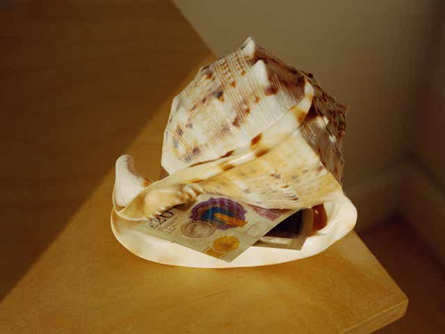 On a table lays a twenty pound note inside a shell.