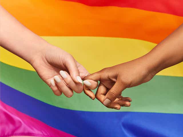 Two women holding hands against the backdrop of the LGBTQ+ pride flag