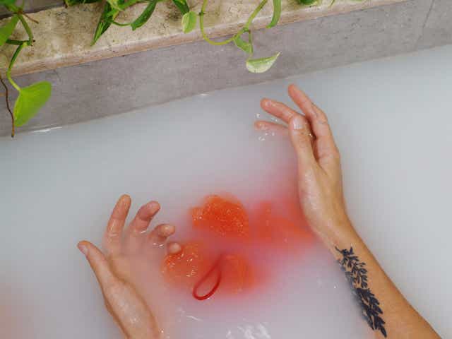 A pair of hands and a red body scrub submerged in bath water.