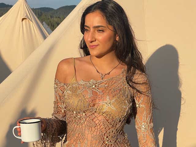 Asal Tehrani holding a mug and wearing a gold bikini top under a cream crochet long-sleeve top.