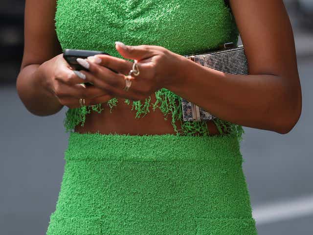 PARIS, FRANCE - JUNE 23: A guest seen wearing a green fringed crop top, matching green fringed midi skirt, gold pendant necklace and a gold leo pattern clutch, outside the Amiri show, during Paris Fashion Week - Menswear Spring/Summer 2023 on June 23, 2022 in Paris, France