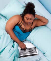 Black woman watches TV on laptop in bed