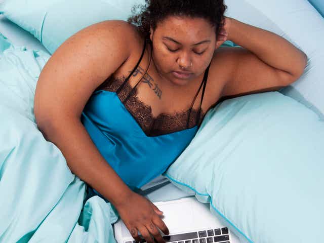 Black woman watches TV on laptop in bed