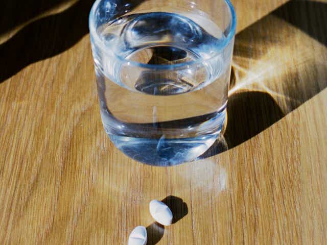 Glass of water and two white pills on a wooden table