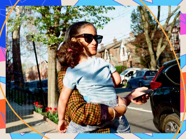 A photo of a brown-skinned female candidate with sunglasses on holding her sleeping baby in her hands while walking