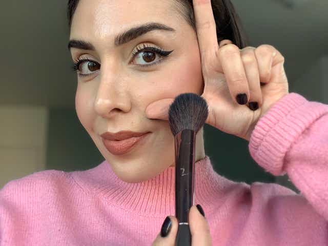 Selfie of Jacqueline with her hand up to her face in an L-shape while holding a blush brush underneath