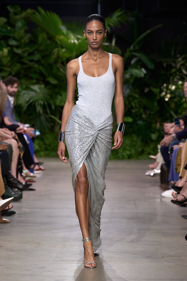 A model wearing a white tank top with a sequin skirt at the Michael Kors Collection Spring 2023 runway.