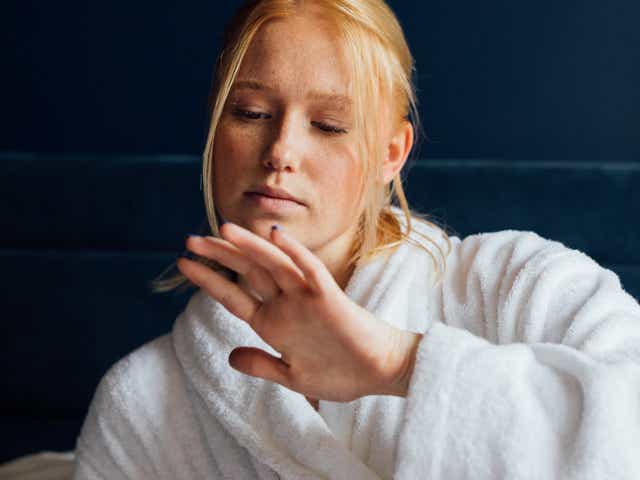 Woman in white bathrobe looking at her manicured nails