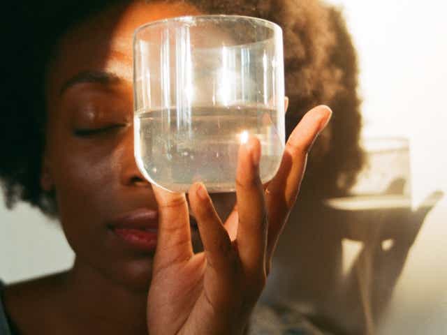Woman with eyes closed holds a glass of water in front of her face