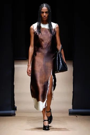 a model wears a white and brown dress with a black tote bag at the prada spring 2023 show