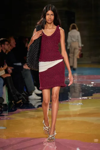 a model wears a red top and skirt set with a black handbag and silver sandals from bottega veneta spring 2023