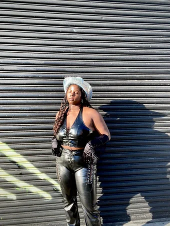 charmaine goodwin wears a silver mirror disc cowboy hat with black leather crop top and matching pants