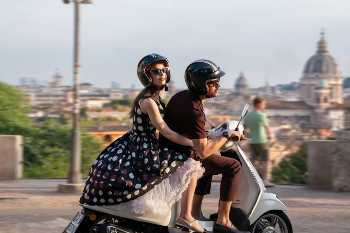 Lily Collins on the back of a vespa wearing a black and white polka dot dress in Emily in Paris season 4