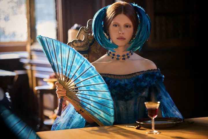 Mia Goth in a blue dress with a feather headpiece and Tiffany & Co. beetle necklace.