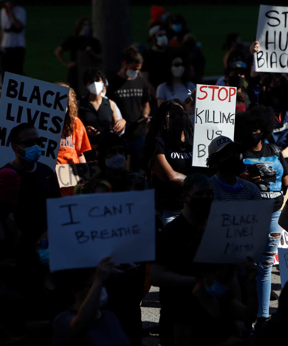 At a Black Lives Matter rally, protestors hold signs that say things including "Black Lives Matter," "I Can't Breathe," and "Stop Killing Us."